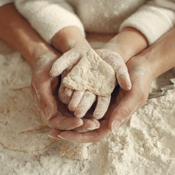 A mother and child bonding through baking, hands covered in flour while making dough.